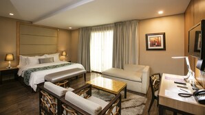 A hotel room with a bed, a desk, a chair, a sofa, and a television. - Goldberry Suites & Hotel Mactan (Lapu-Lapu)