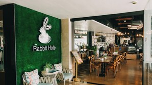 A restaurant interior with a green wall, a sign reading "The Rabbit Hole," and a dining area with wooden chairs and tables. - Goldberry Suites & Hotel Mactan (Lapu-Lapu)