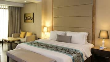 Una camera d'albergo con un letto grande, un comodino con una lampada, una sedia, un tavolino e un quadro appeso al muro.