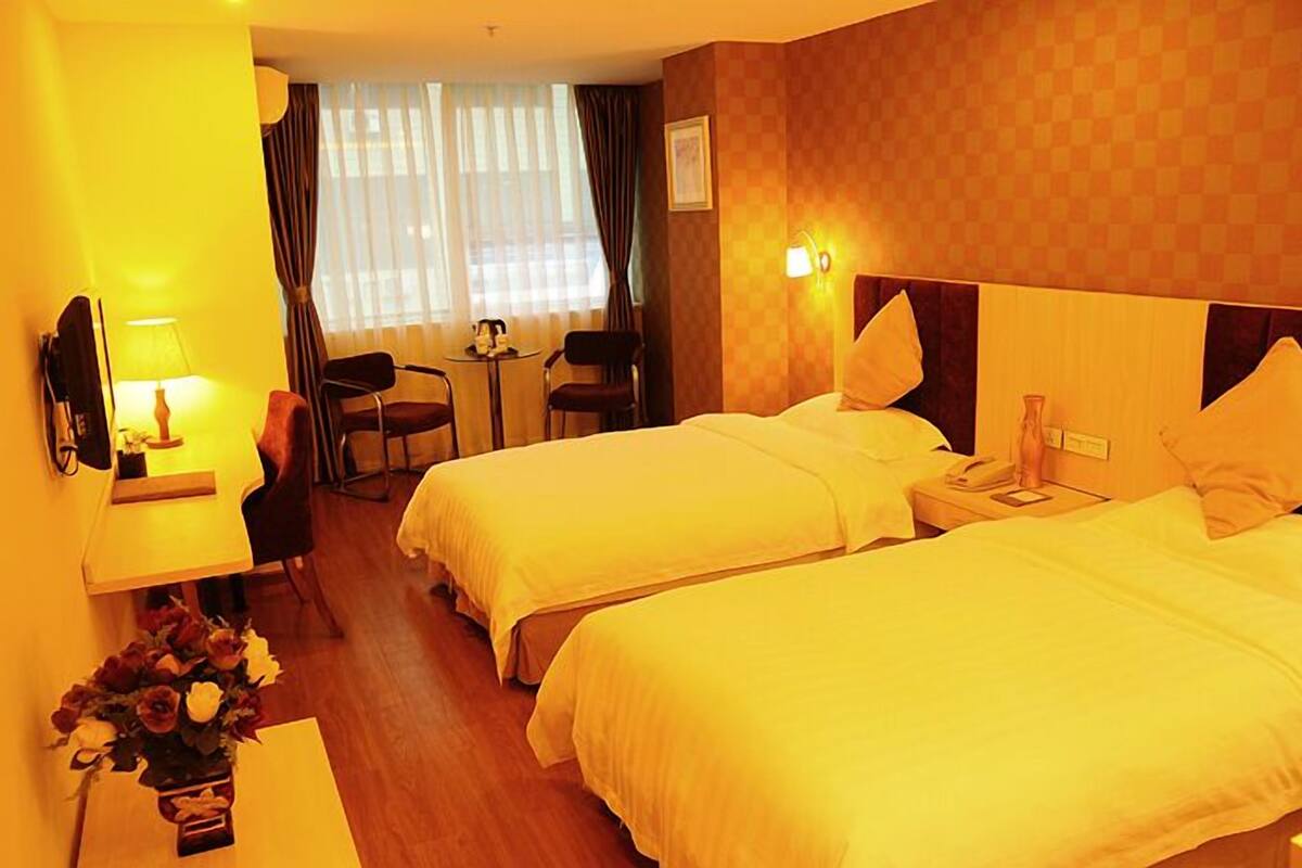 A hotel room with two beds, a desk, a chair, a small table, and a window with curtains.