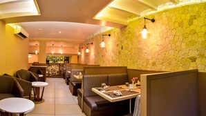 Un restaurant avec des banquettes et des tables, un bar au fond de la salle et un mur en pierre.