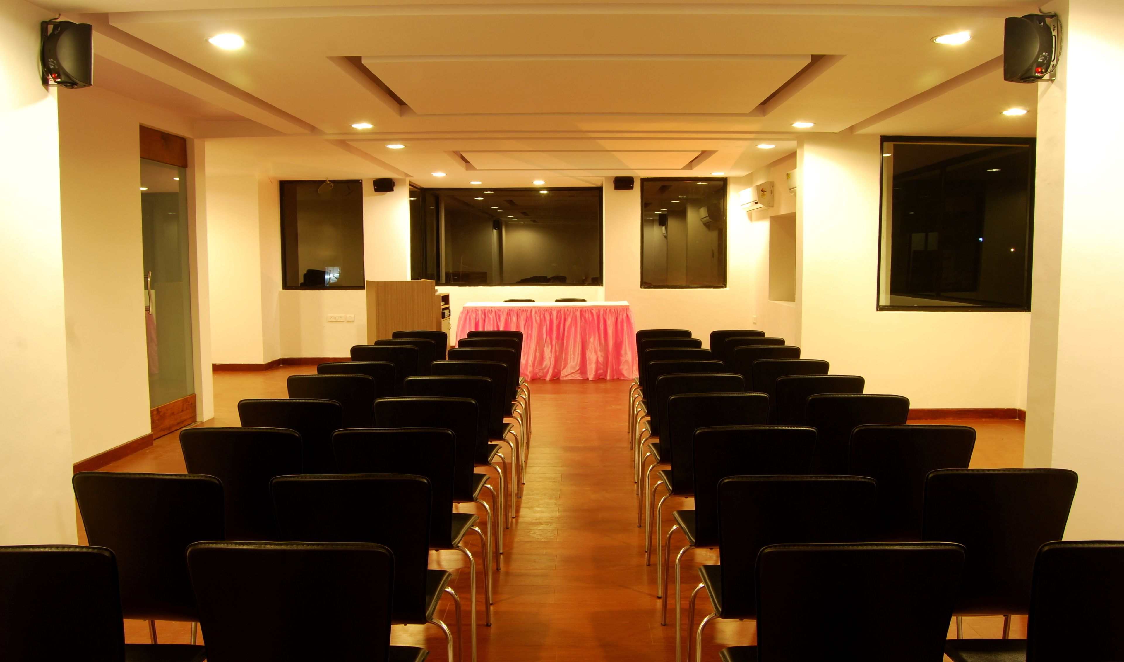 Un salón de conferencias con filas de sillas orientadas hacia una mesa cubierta con un mantel rosa.