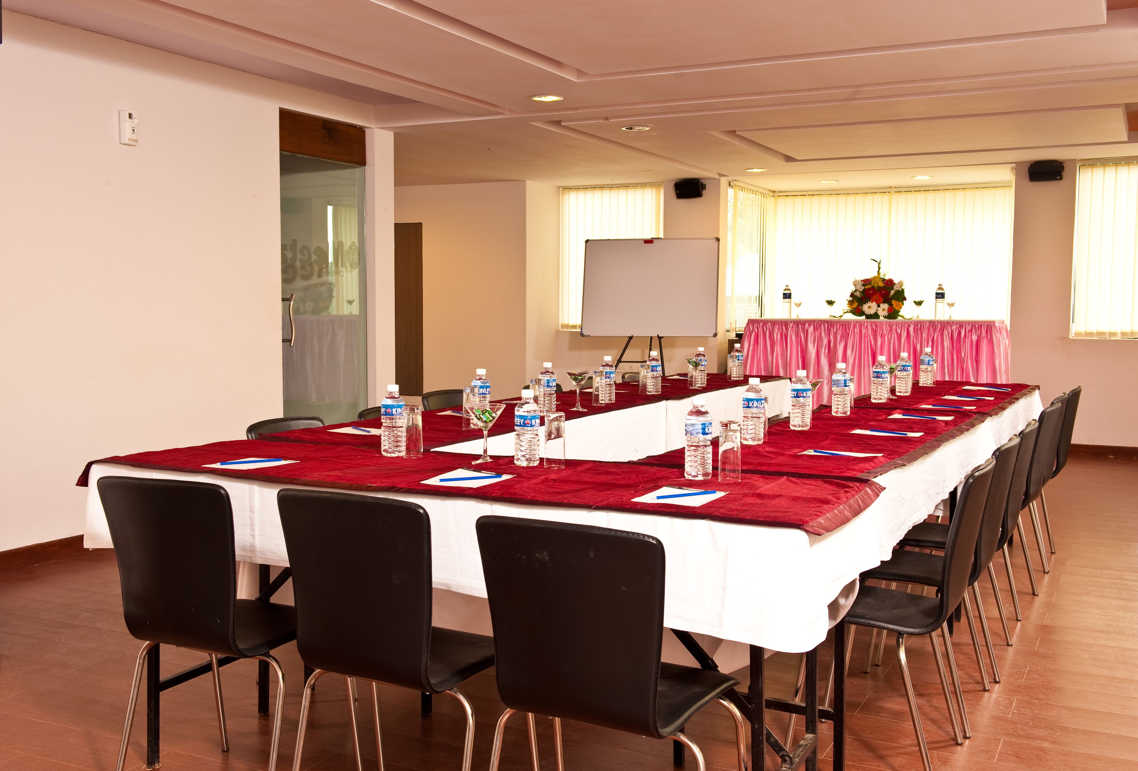 Un salón de conferencias con una larga mesa, sillas negras, botellas de agua y una pizarra.