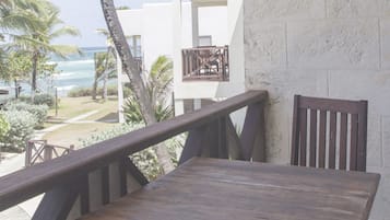 A balcony with a wooden table and chairs, overlooking a beach and palm trees.