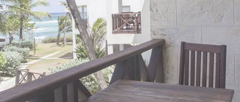 Un balcon avec une table et des chaises en bois, donnant sur une plage et des palmiers.