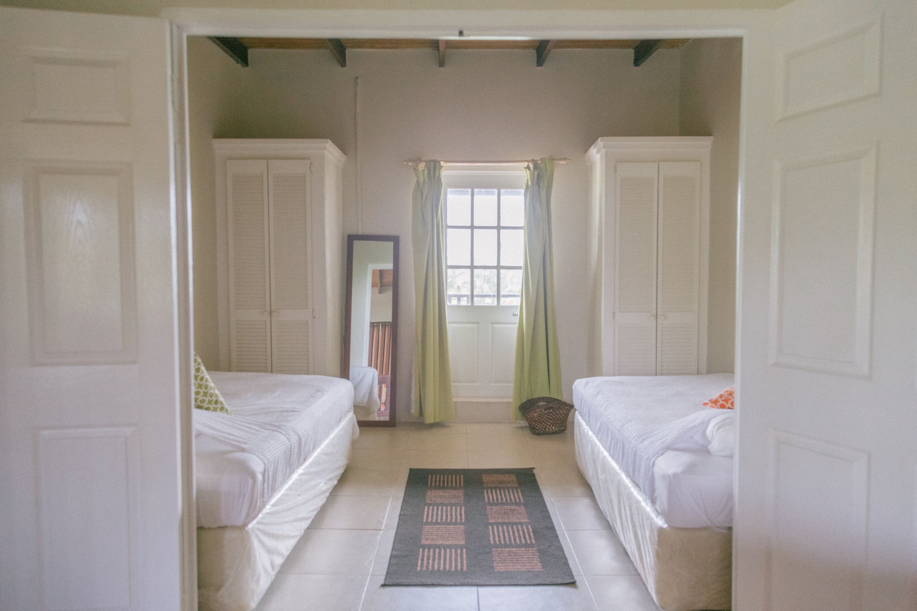 Un dormitorio con dos camas individuales, una ventana con cortinas y un espejo en la pared.