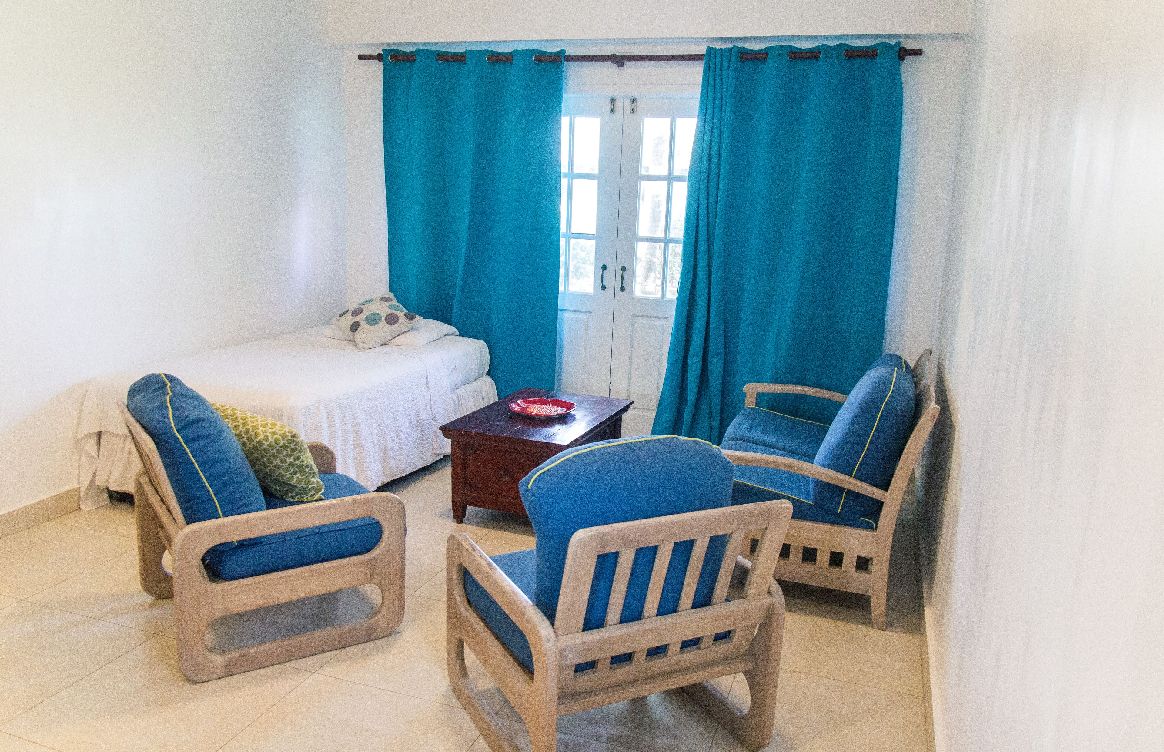 A small, cozy room with a bed, two wooden chairs, a small table, and a window with curtains.