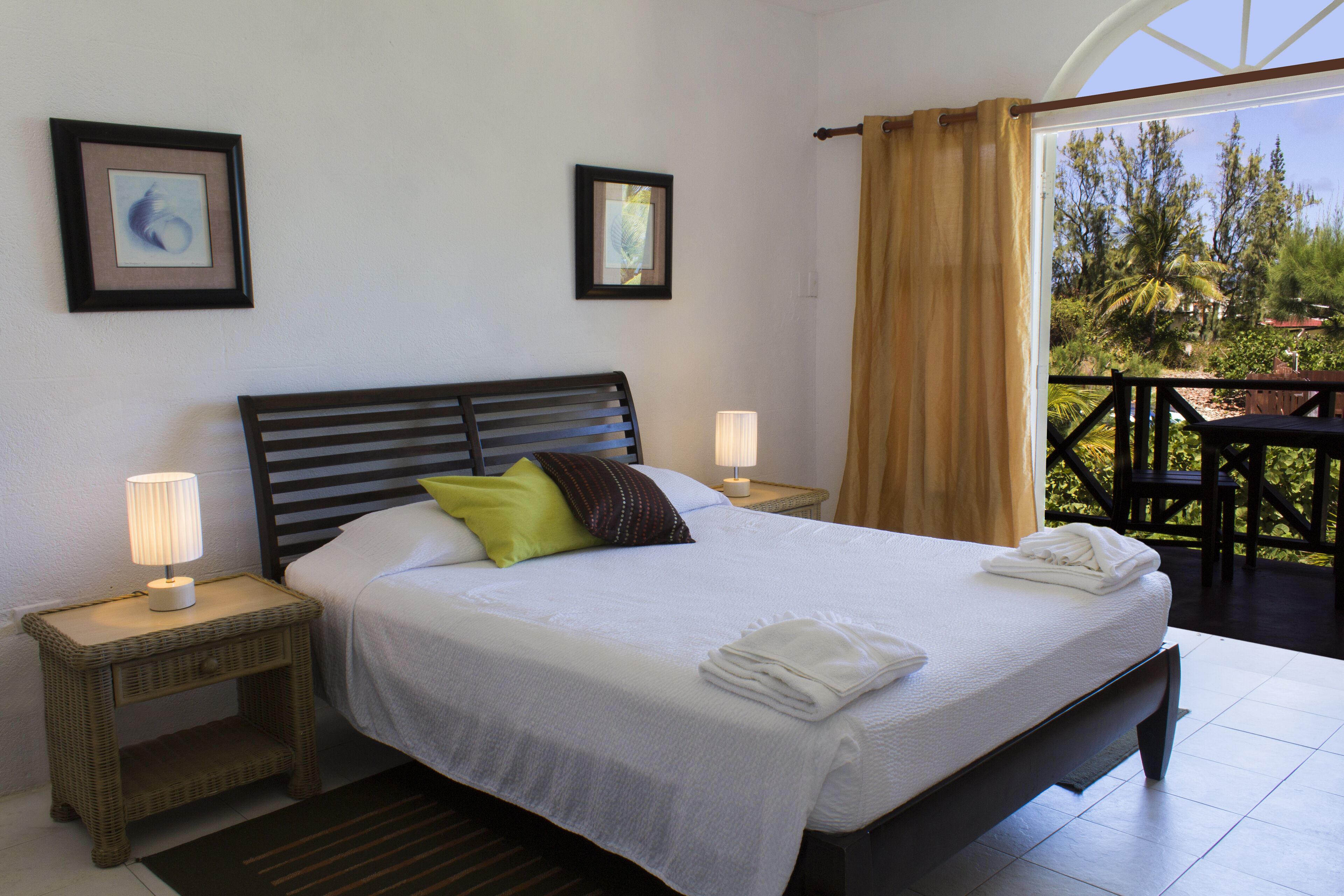 A neatly made bed with white linens and a green pillow, two bedside lamps, and a framed picture on the wall.