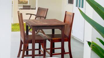 A patio with a wooden table and chairs, a small garden area, and a white wall with a window.