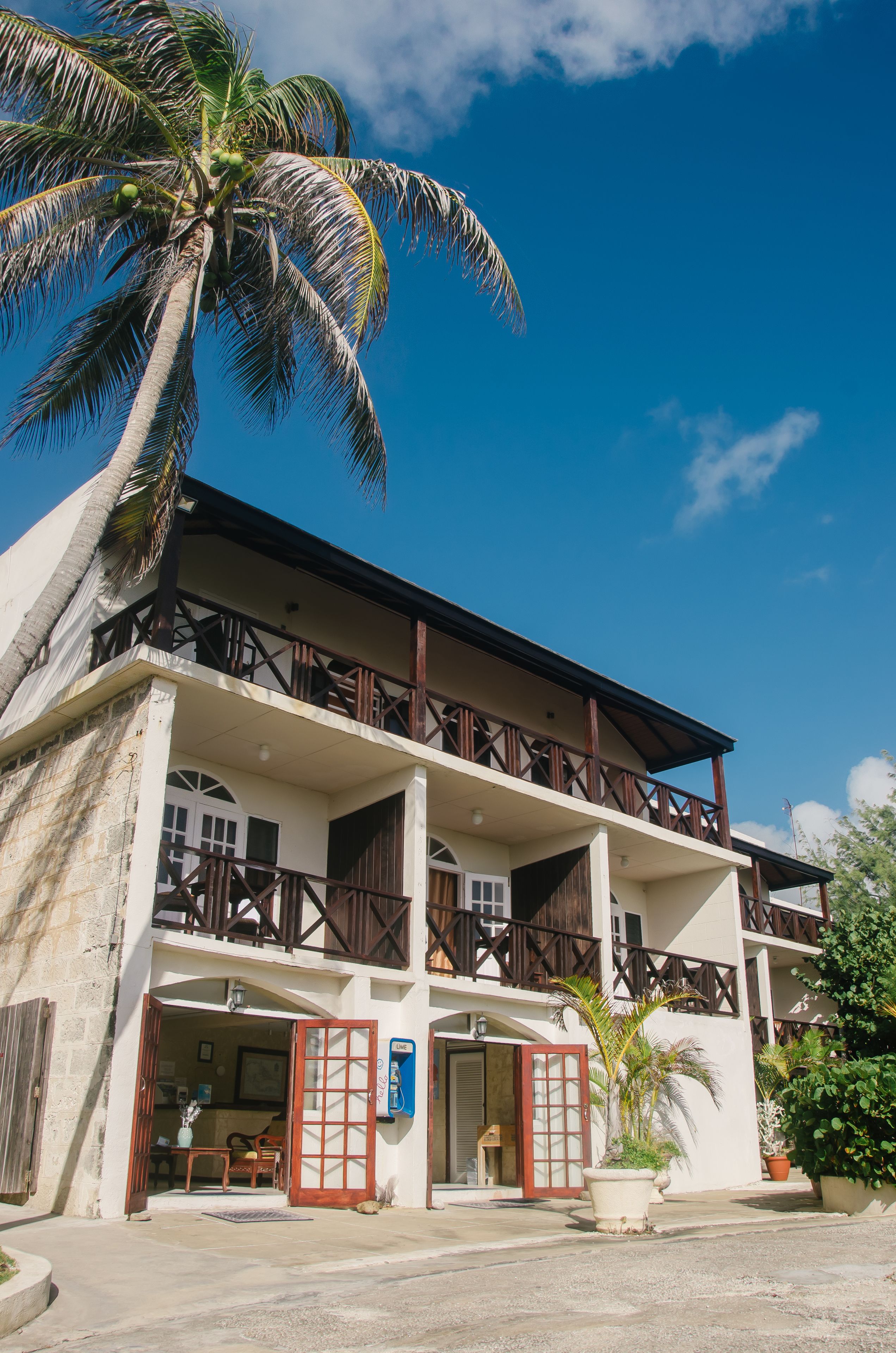 A two-story building with a balcony, a palm tree, and a door with a glass panel.