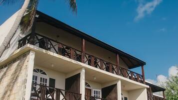 A two-story building with a balcony, a palm tree, and a door with a glass panel.