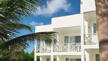 Un edificio blanco de dos pisos con balcones, un césped y una palmera.