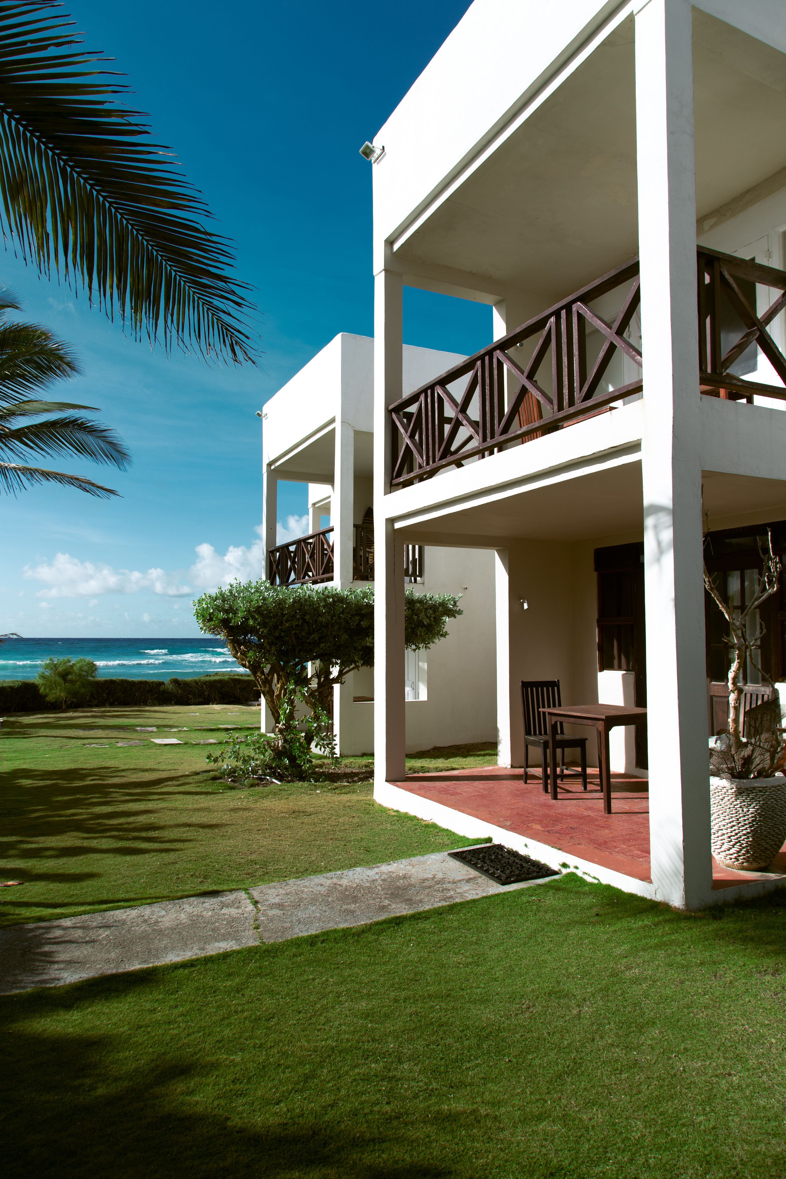 A two-story building with a balcony, a lawn, and a view of the ocean.