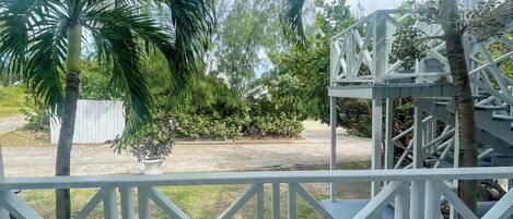 A view from a balcony with a white railing, overlooking a garden with palm trees and a white structure.