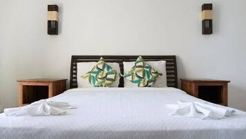 Un lit bien fait, recouvert d’une couvre-lit blanche et agrémenté de deux coussins décoratifs, avec deux tables de chevet en bois de chaque côté.