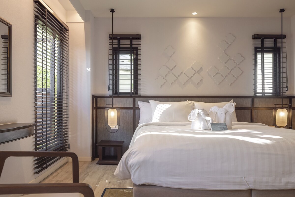 Un dormitorio moderno con una cama grande, dos lámparas fijadas a la pared y una ventana con persianas.