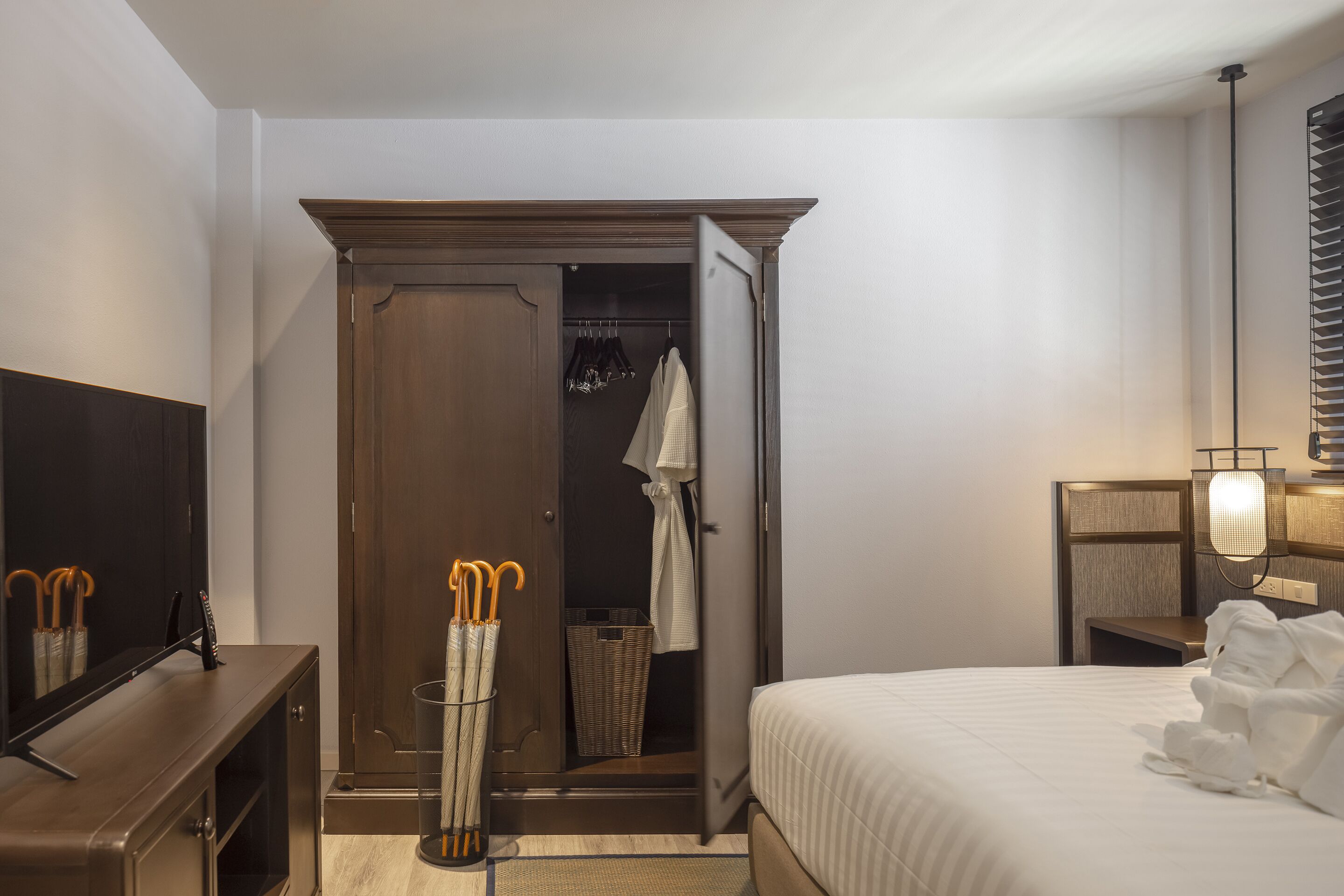 A hotel room with a bed, a wardrobe, a mirror, a TV, and a lamp.