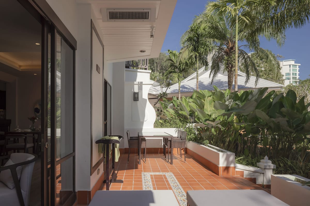 A patio with a dining table and chairs, surrounded by plants and a palm tree.