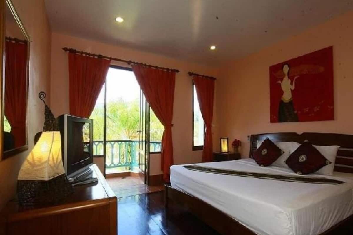 A bedroom with a bed, a desk with a lamp, a window with curtains, and a painting on the wall.