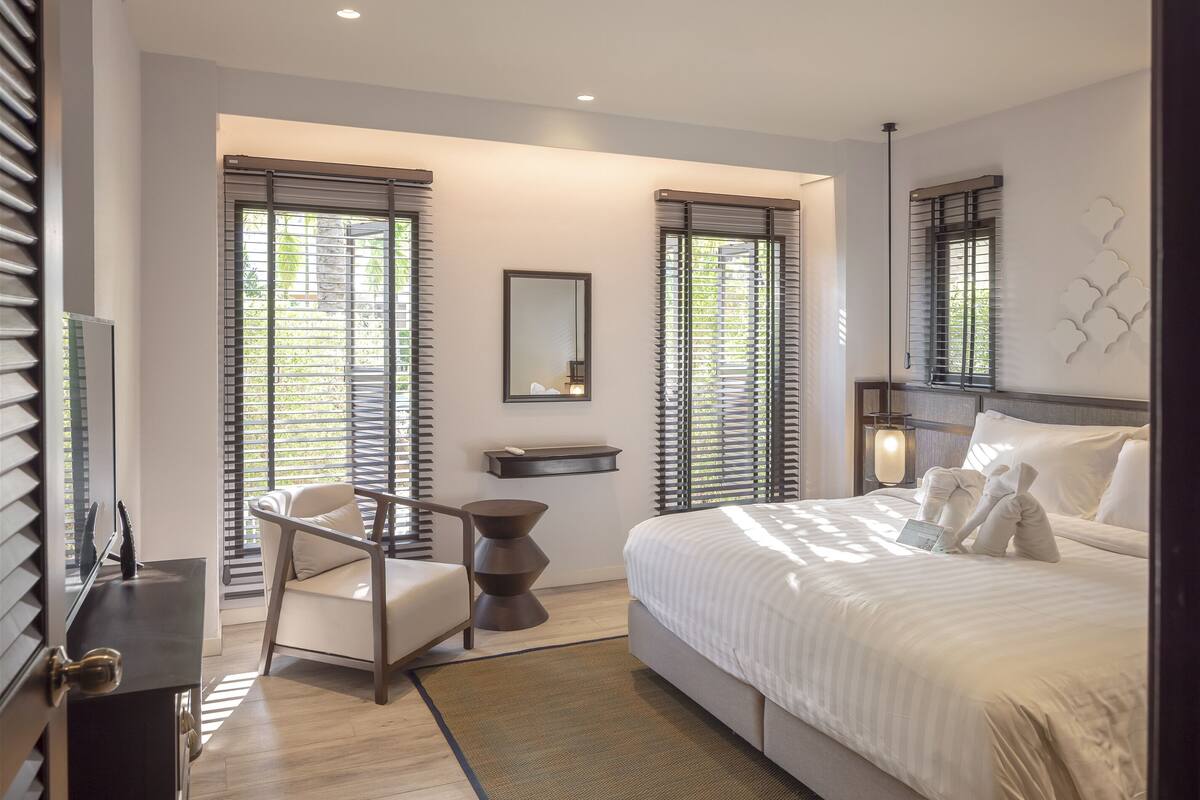A modern hotel room with a large bed, a desk, a chair, and a small side table.