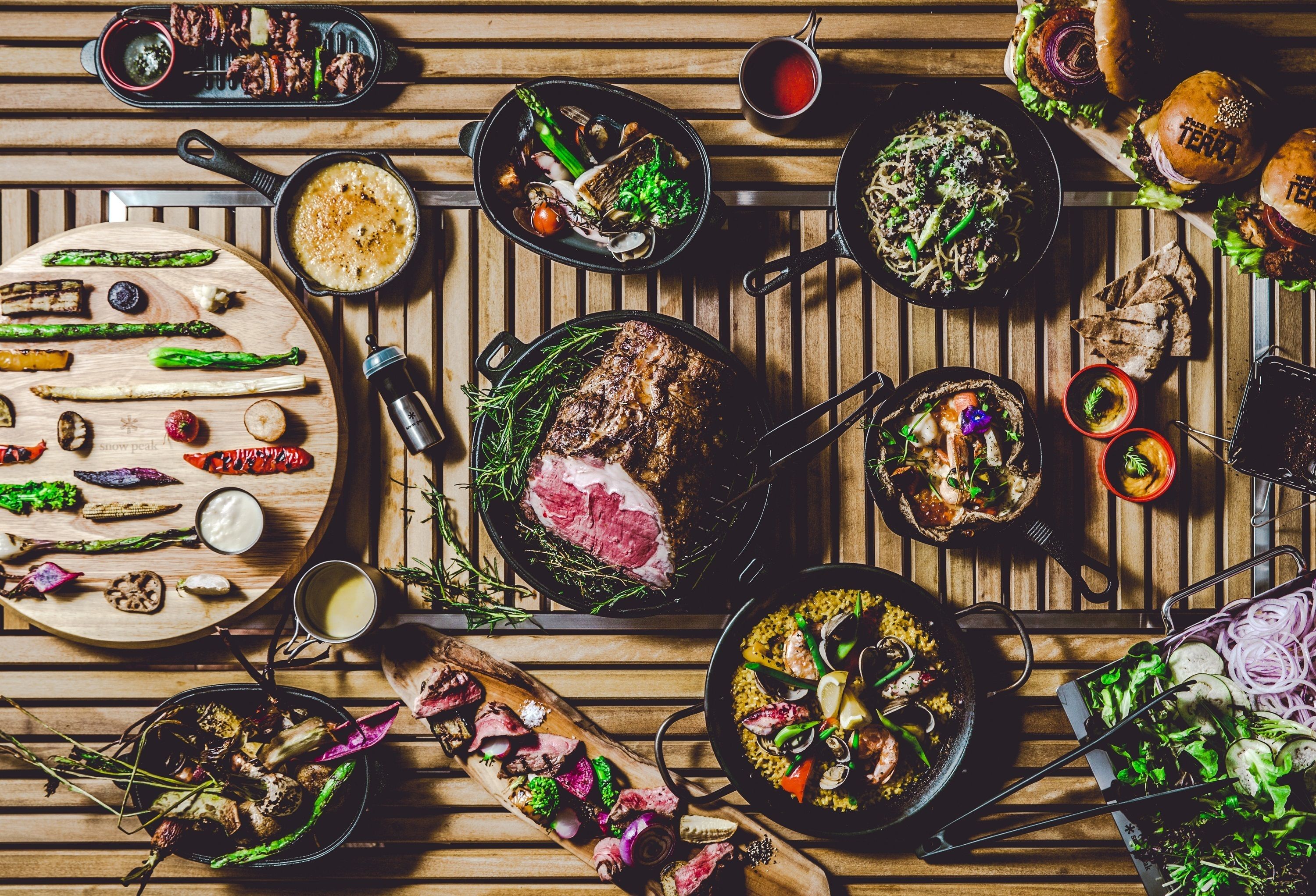 Una variedad de platos sobre una mesa de madera, con carnes a la parrilla, mariscos y verduras.