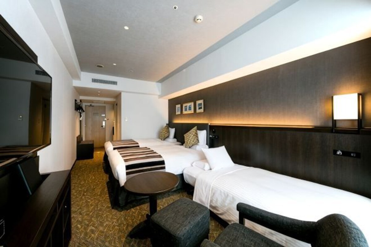A hotel room with two beds, a TV, a desk, and a sofa.