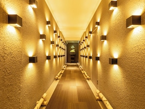 Een gang met gestructureerde wanden, inbouwverlichting en een houten vloer.