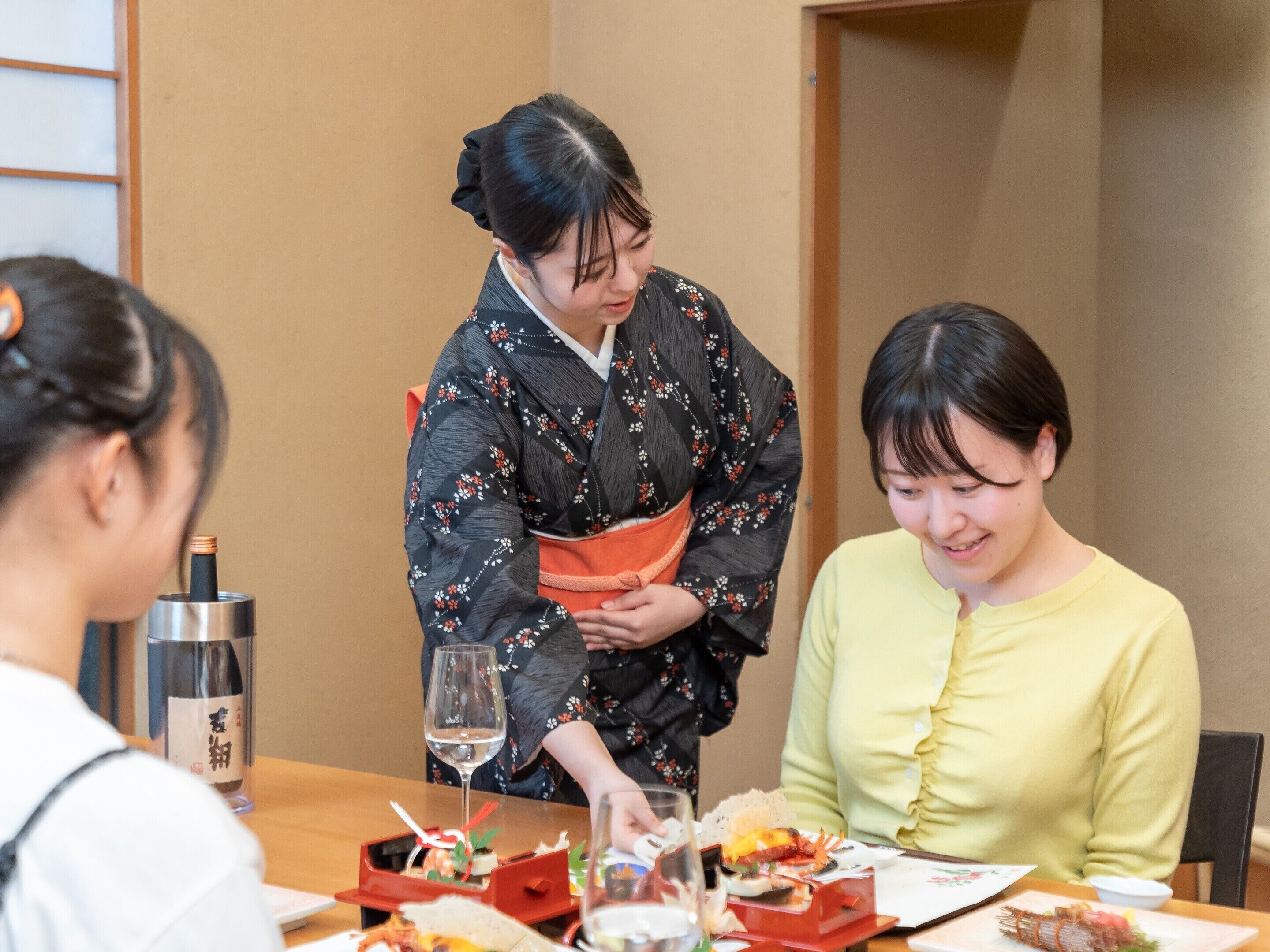 A traditional Japanese setting with a table set for a meal, a person in a kimono, and a bottle with Japanese characters.