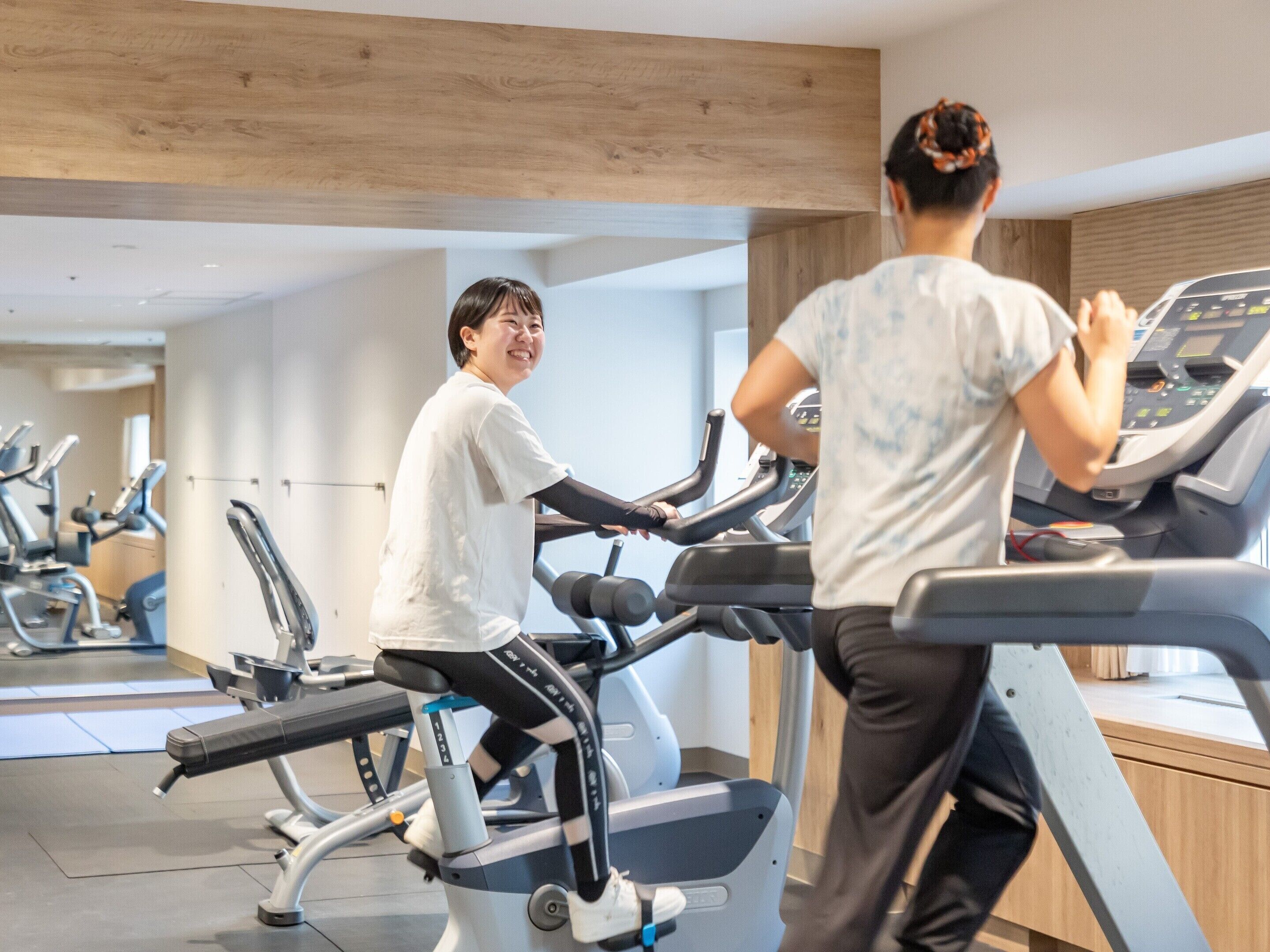 A gym with exercise equipment, a mirrored wall, and a wooden ceiling.