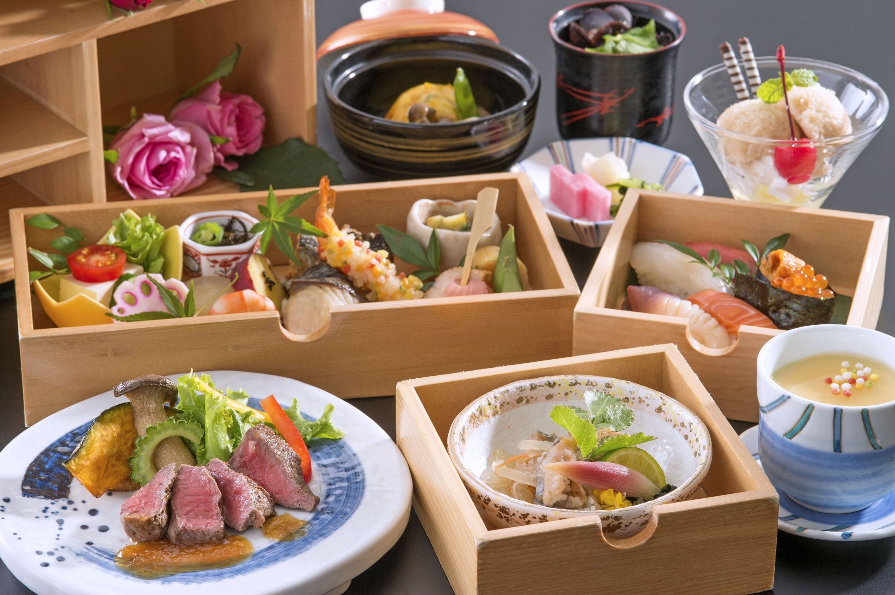 Variedad de platos japoneses en cajas y recipientes de madera, incluyendo sushi, sashimi y un tazón de sopa.