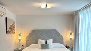 A neatly made bed with a tufted headboard, two bedside lamps, and a painting on the wall. - Colombe Hotel Boutique (Xalapa)