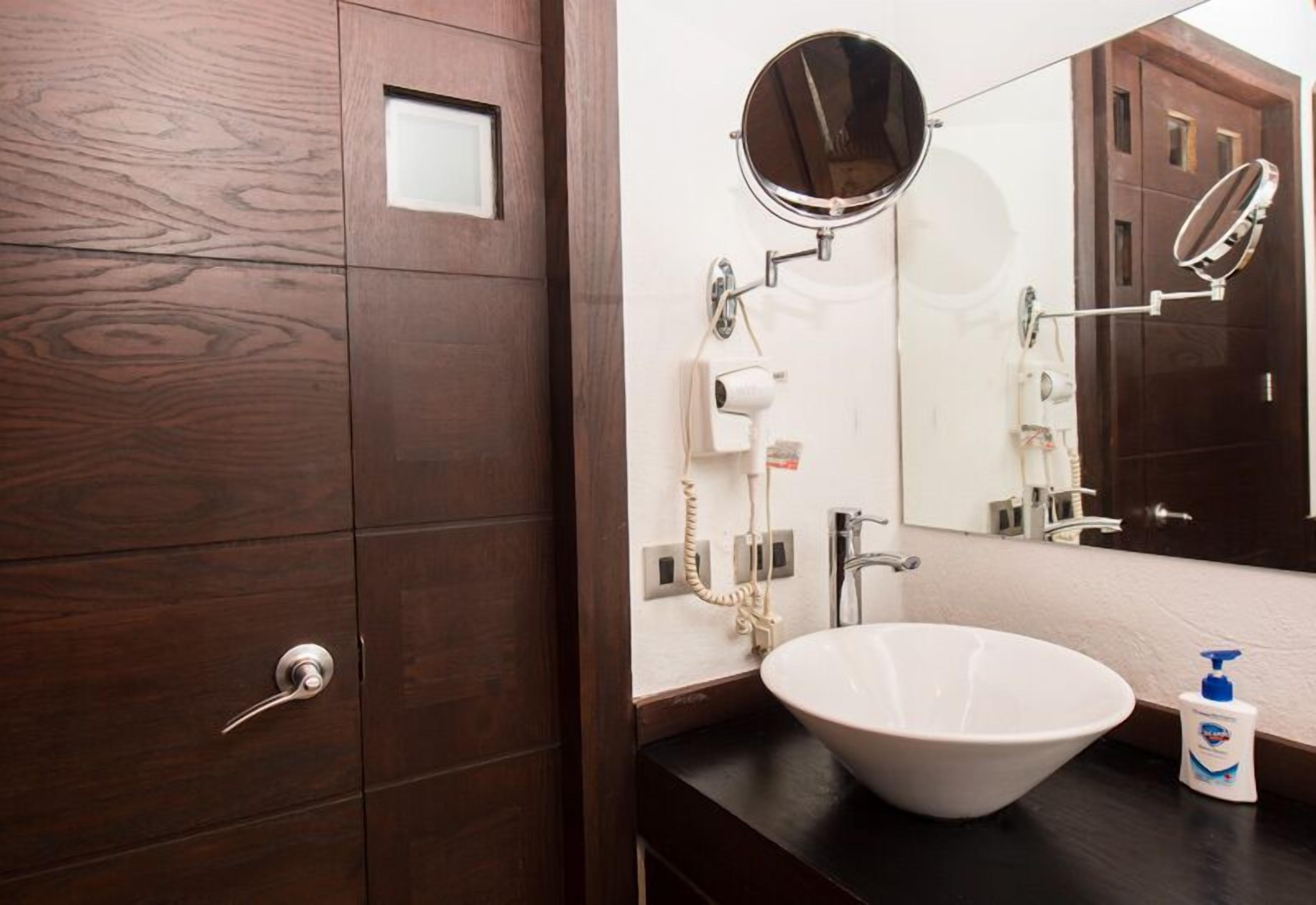 Un baño con puerta de madera, un lavabo blanco, un espejo y un secador de manos.