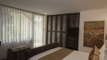 A hotel room with a bed, a chest of drawers, a painting on the wall, and a window with sheer curtains.