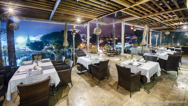 An outdoor restaurant with tables set for dining, wicker chairs, and a view of the cityscape at night. - Colombe Hotel Boutique (Xalapa)