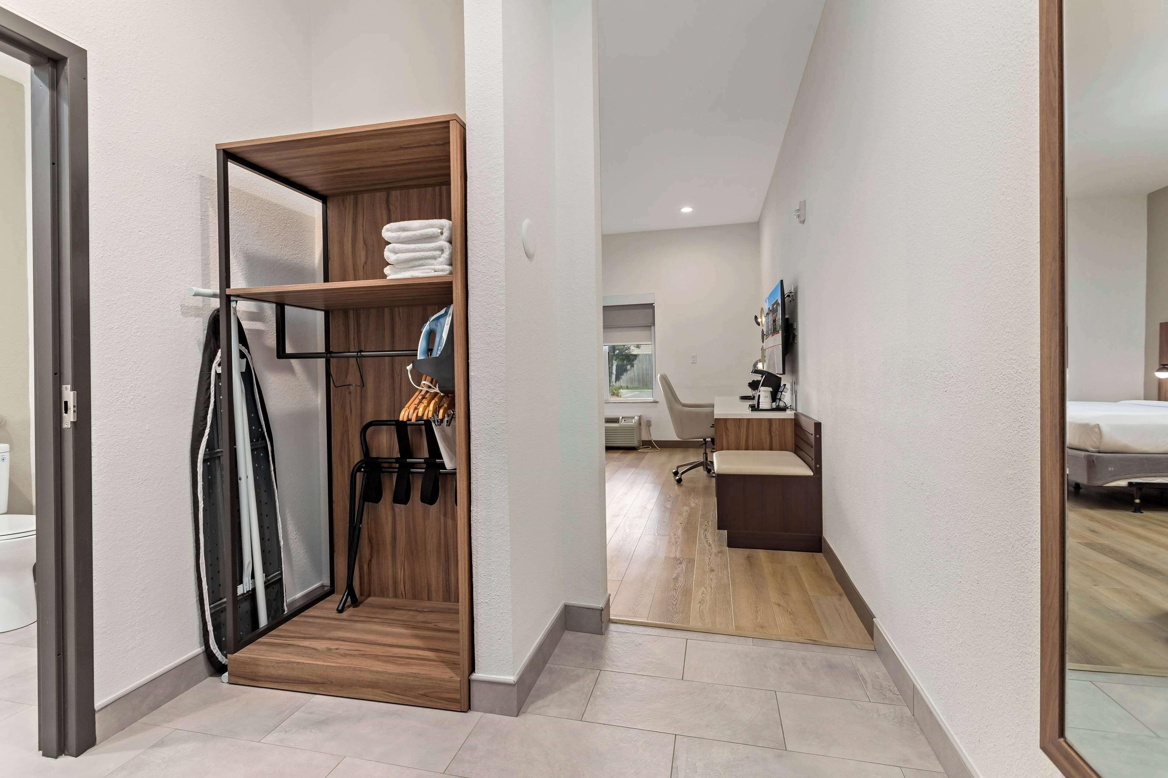 A hotel room with a wooden wardrobe, a desk, a chair, and a bed.