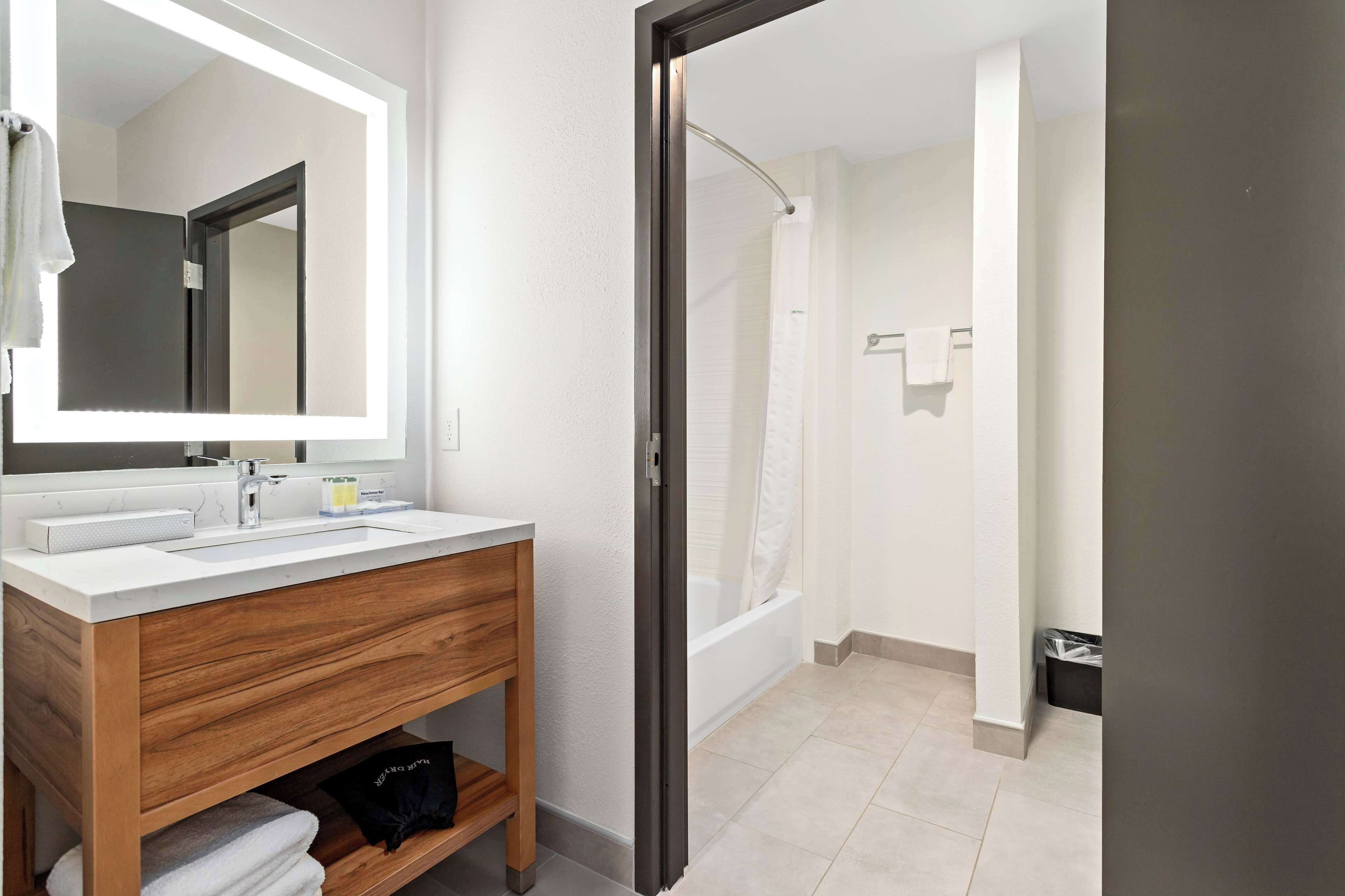 A modern bathroom with a wooden vanity, a large mirror, and a separate shower area.