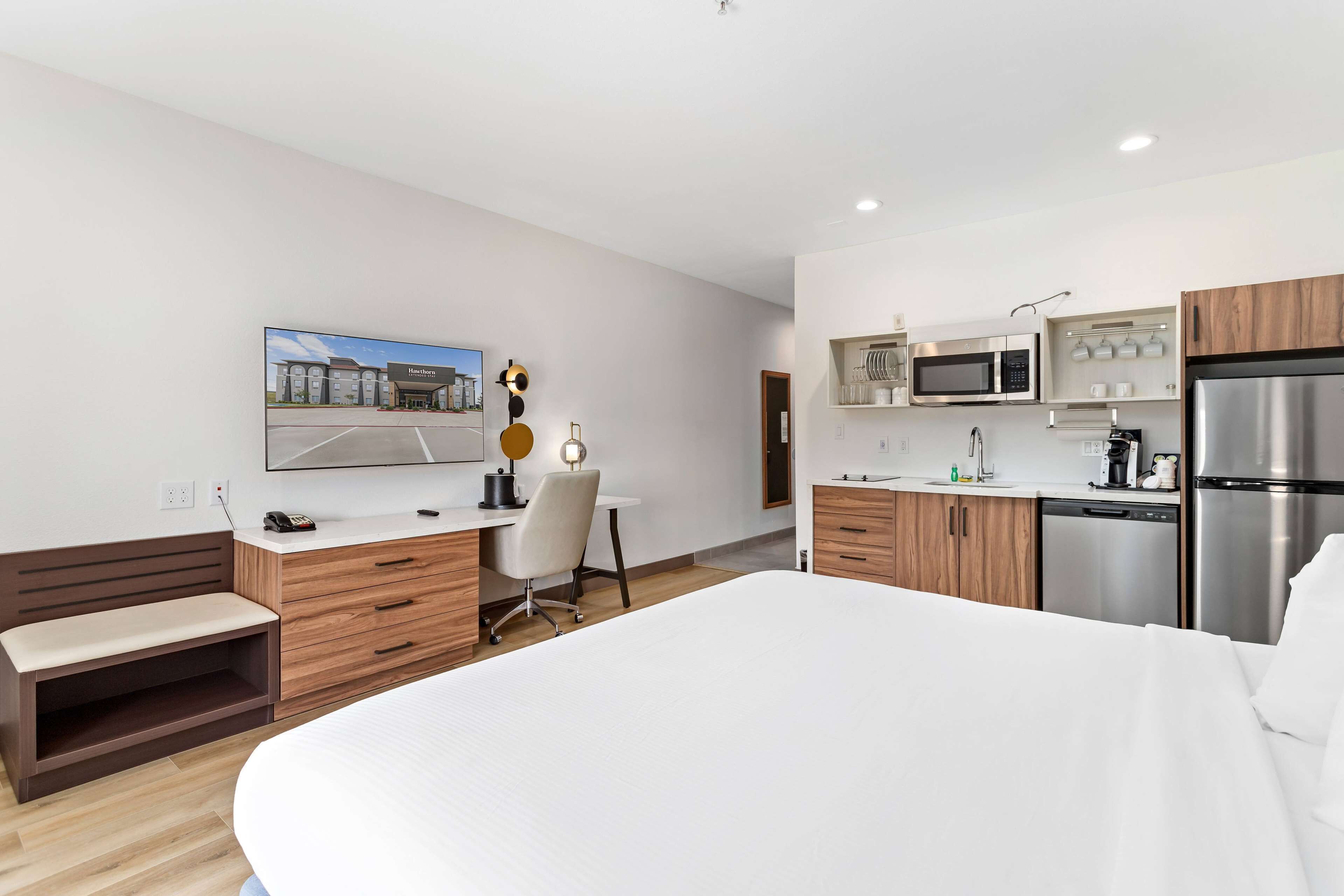 Une chambre d’hôtel moderne dotée d’un grand lit, d ’un bureau avec une chaise, d’une télévision à écran plat et d’une kitchenette équipée d’un four à micro-ondes, d’une machine à café et d’un réfrigérateur.