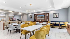 Un restaurant moderne avec des chaises jaunes et grises, des tables blanches et un coin salon bleu.