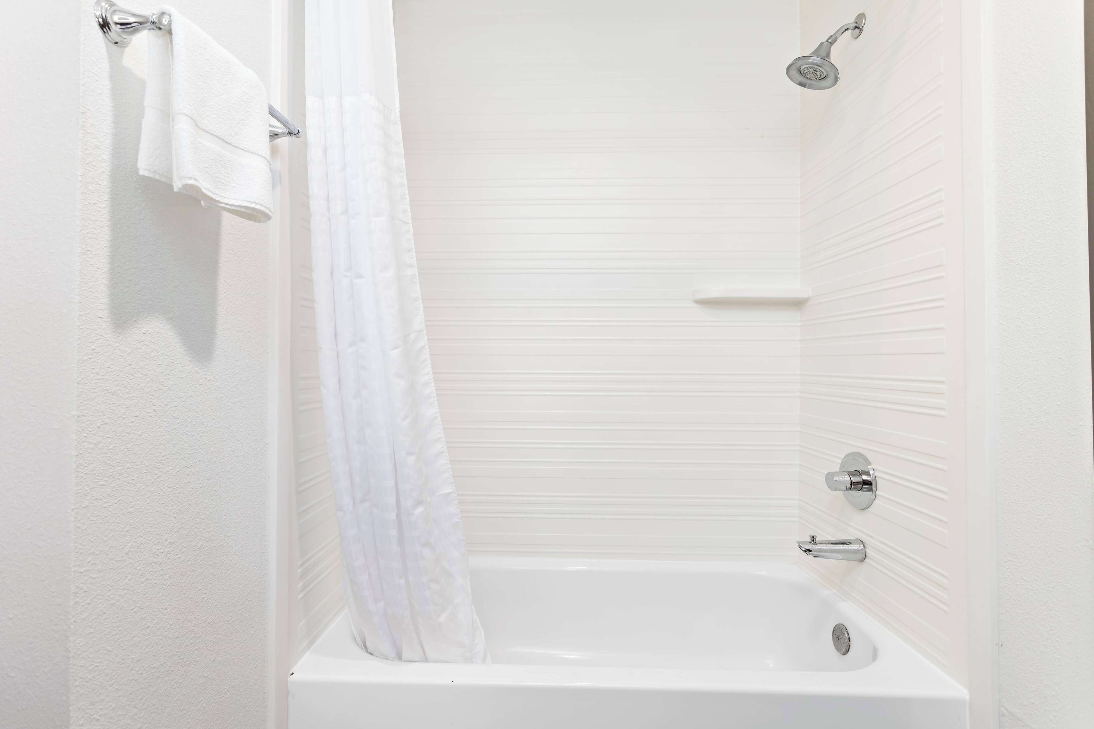 Un baño blanco con bañera, ducha y barra para toallas.