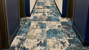 Un long couloir étroit d’hôtel, avec un tapis à motifs, des portes des deux côtés et un éclairage au plafond.