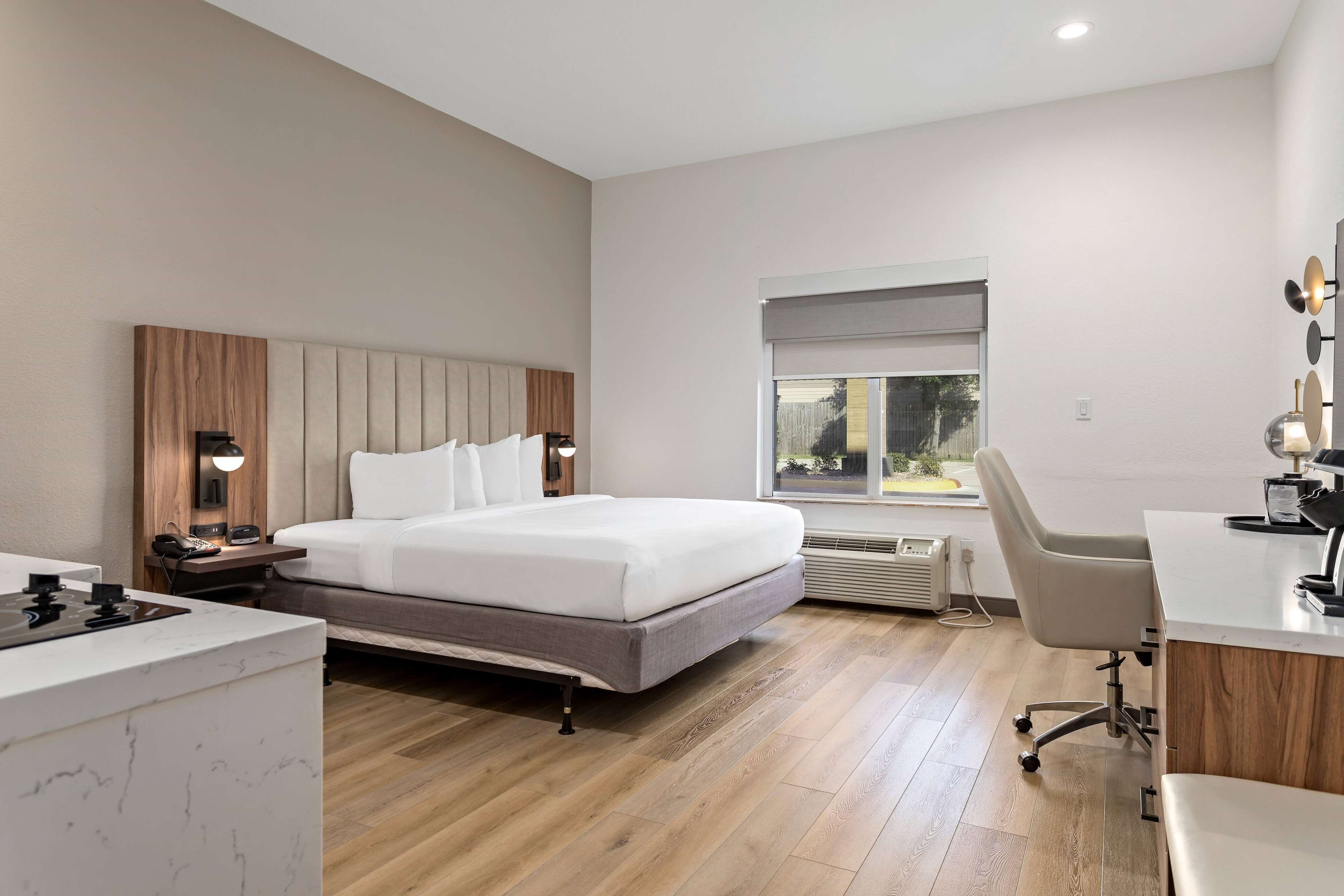 Een moderne hotelkamer met een bed, nachtkastje, bureau, stoel en een raam met uitzicht.