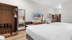 Une chambre d’hôtel comprenant une armoire en bois, un lit, un bureau avec une chaise, un four à micro-ondes, un réfrigérateur et un grand miroir.