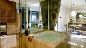 A modern bathroom with a large bathtub, a glass shower enclosure, and a visible dining area in the background. - Hepburn at Hepburn (Hepburn Springs)