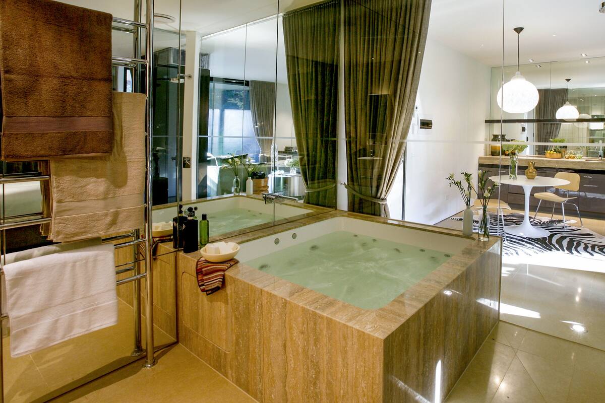 A modern bathroom with a large bathtub, a glass shower enclosure, and a visible dining area in the background.