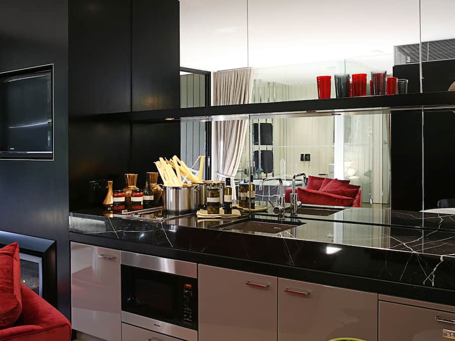 Una cocina moderna con encimera negra, electrodomésticos de acero inoxidable y una silla roja.