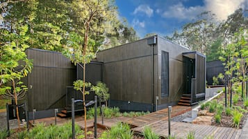 Una casa moderna e minimalista con un patio in legno, immersa nel verde e circondata da alberi.