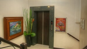 Um saguão de hotel com uma escada, um quadro emoldurado, um vaso de planta, um cartaz e uma luminária no teto.