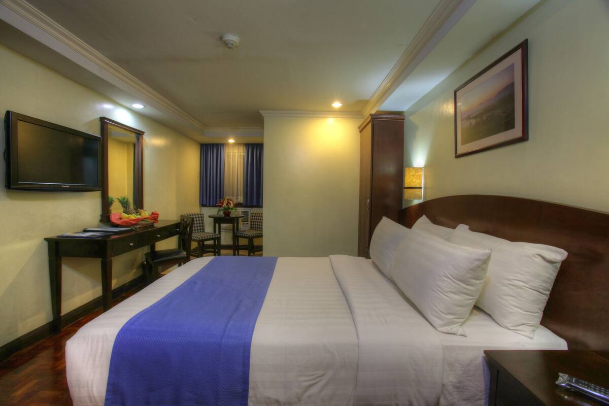 A hotel room with a large bed, a desk with a chair, a television, and a framed picture on the wall.