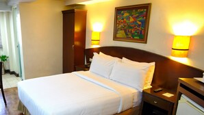 Quarto de hotel com uma cama grande, luminárias de cabeceira, mesa de cabeceira, um pequeno frigorífico e um quadro na parede.