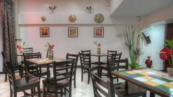A dining area with multiple tables and chairs, a tiled floor, and wall decorations including framed pictures and wall-mounted items.